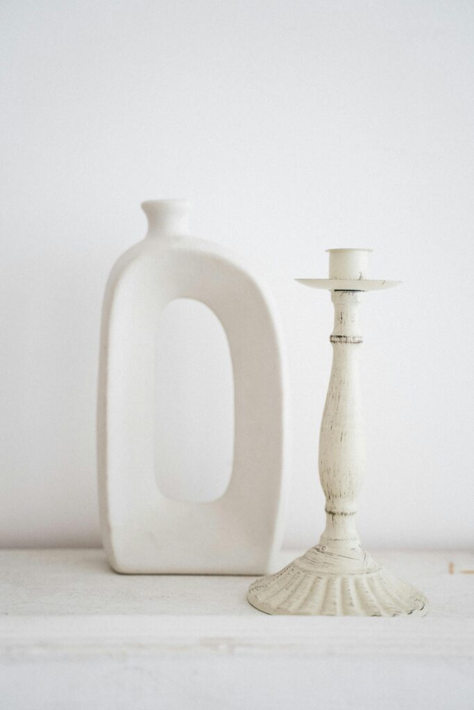 A minimalist composition of a ceramic vase and vintage candlestick against a white background, embodying simplicity and elegance.